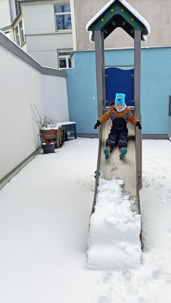 Ein Kind der CVJM-Kita Oberbarmen auf der schneebedeckten Rutsche