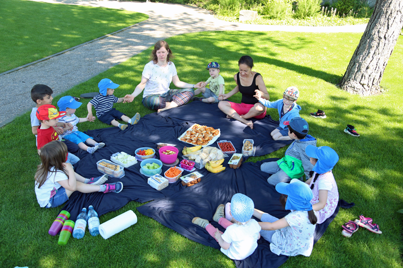 Kinder und Erzieherinnen beim Picknick-Frühstück
