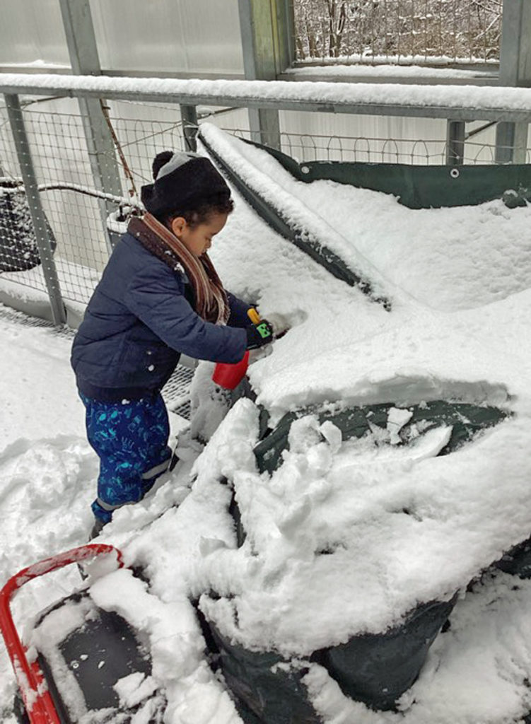ein kind entfernt den schnee von kleinen fahrzeugen