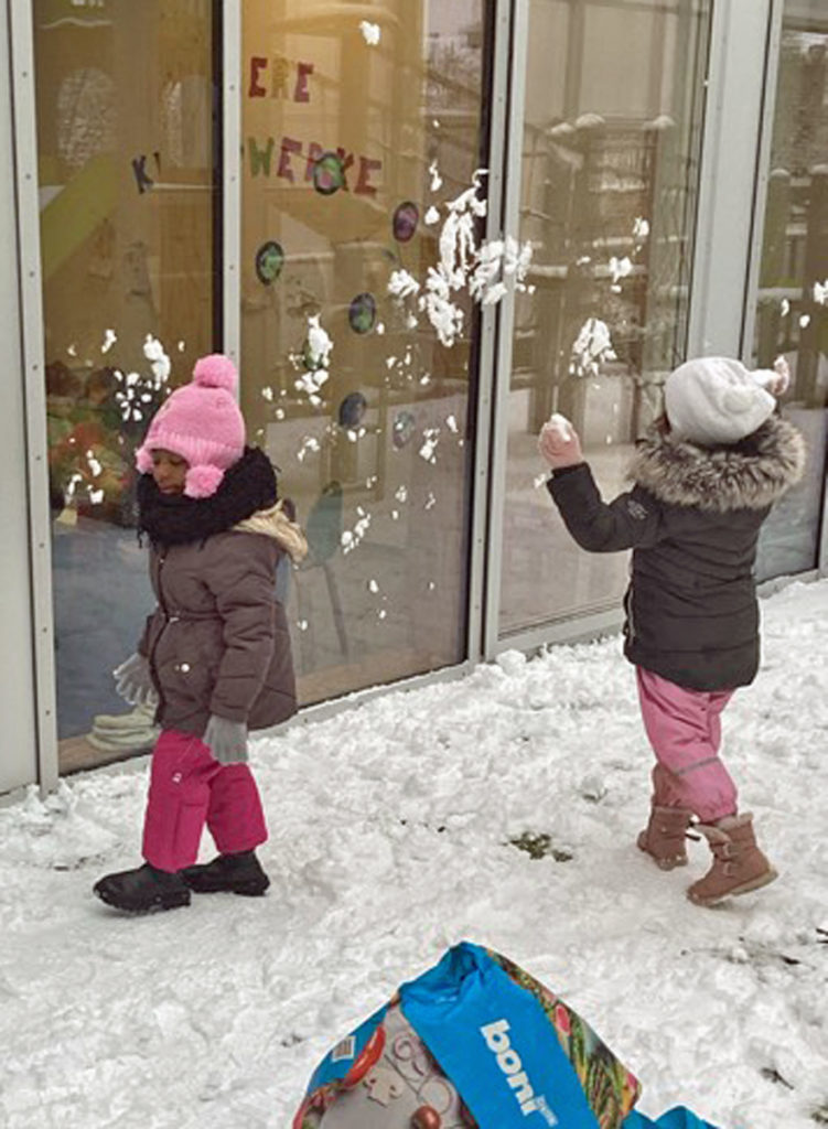 zwei kinder werfen schneebaelle gegen eine fensterfront