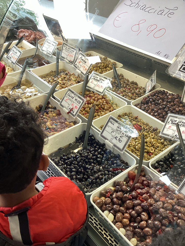 ein-junge-steht-vor-einer-theke-mit-vielen-olivenschuesseln