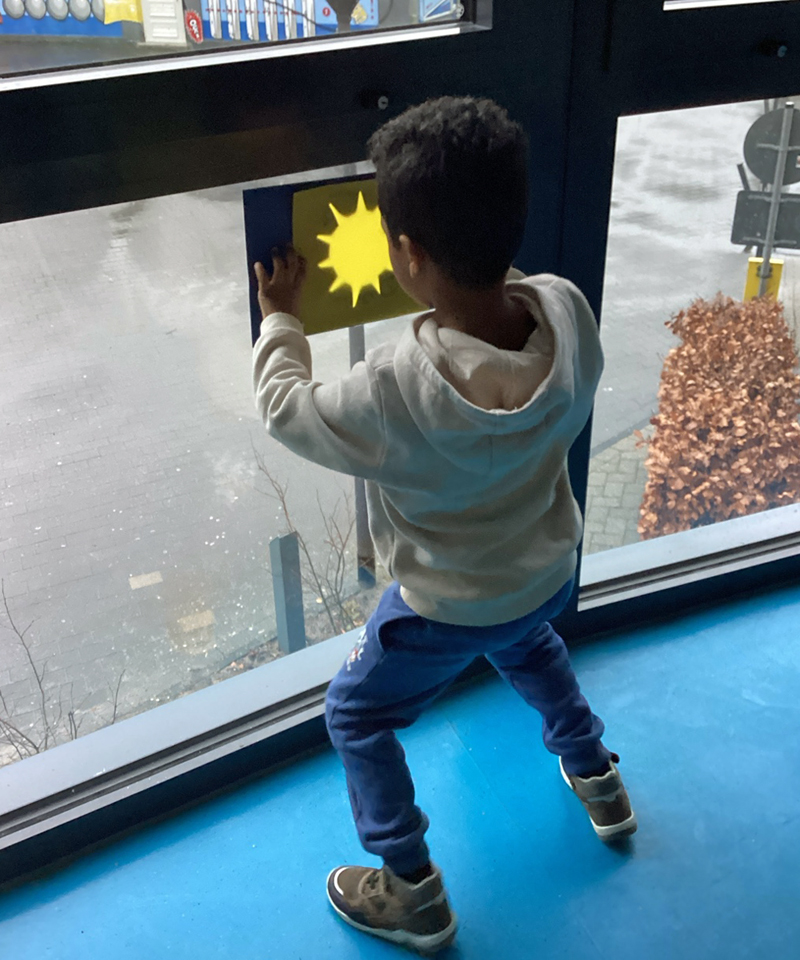 Ein Junge haelt ein Transparentbild mit einer Sonne an eine Fensterscheibe