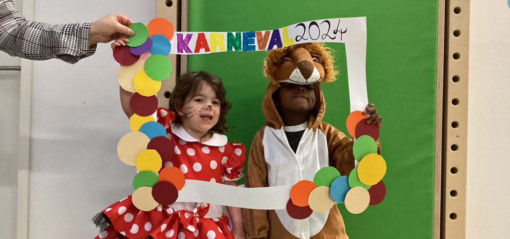 Zwei Kinder halten einen Papprahmen mit der Aufschrift Karneval 2024 hoch