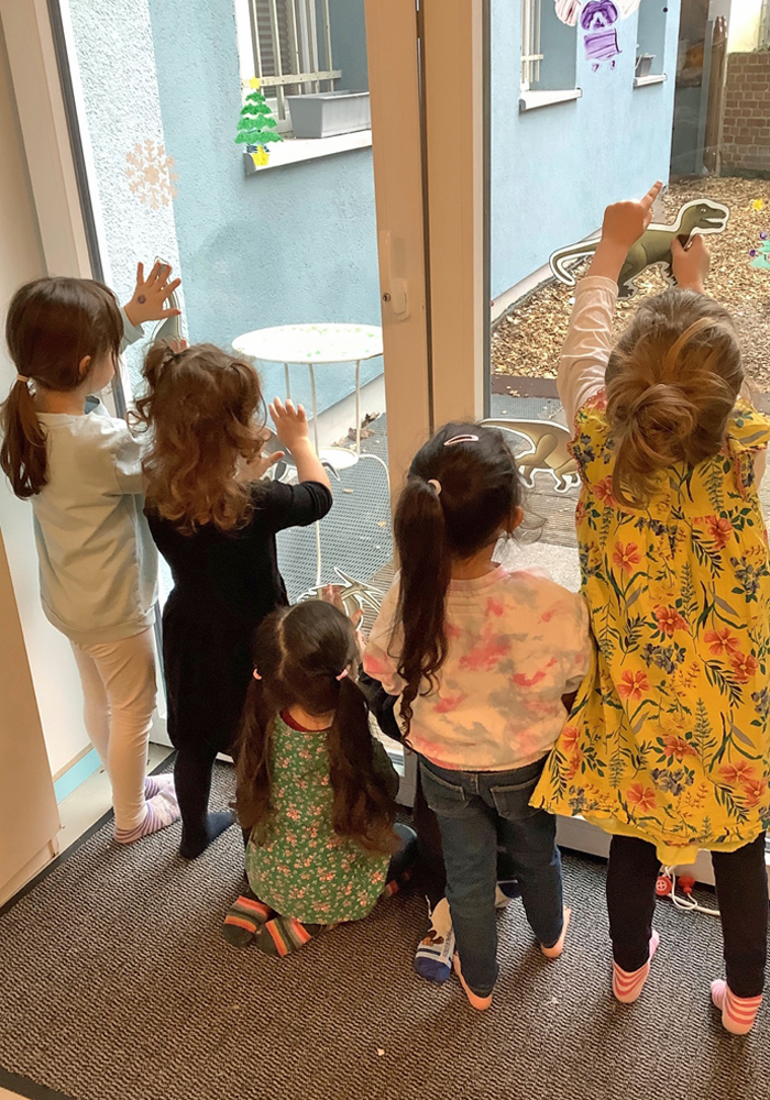Kinder bringen Dinosaurier-Fensterbilder an den Scheiben der Kita an