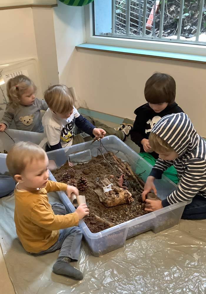 Kinder gestalten mit Naturmaterialien eine Dino-Landschaft in einer großen Plastikwanne