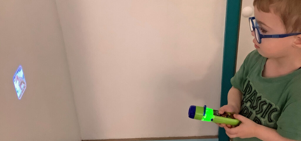 Ein Kind zaubert mit einem Taschenlampenprojektor einen Dinosaurier auf die Zimmerwand