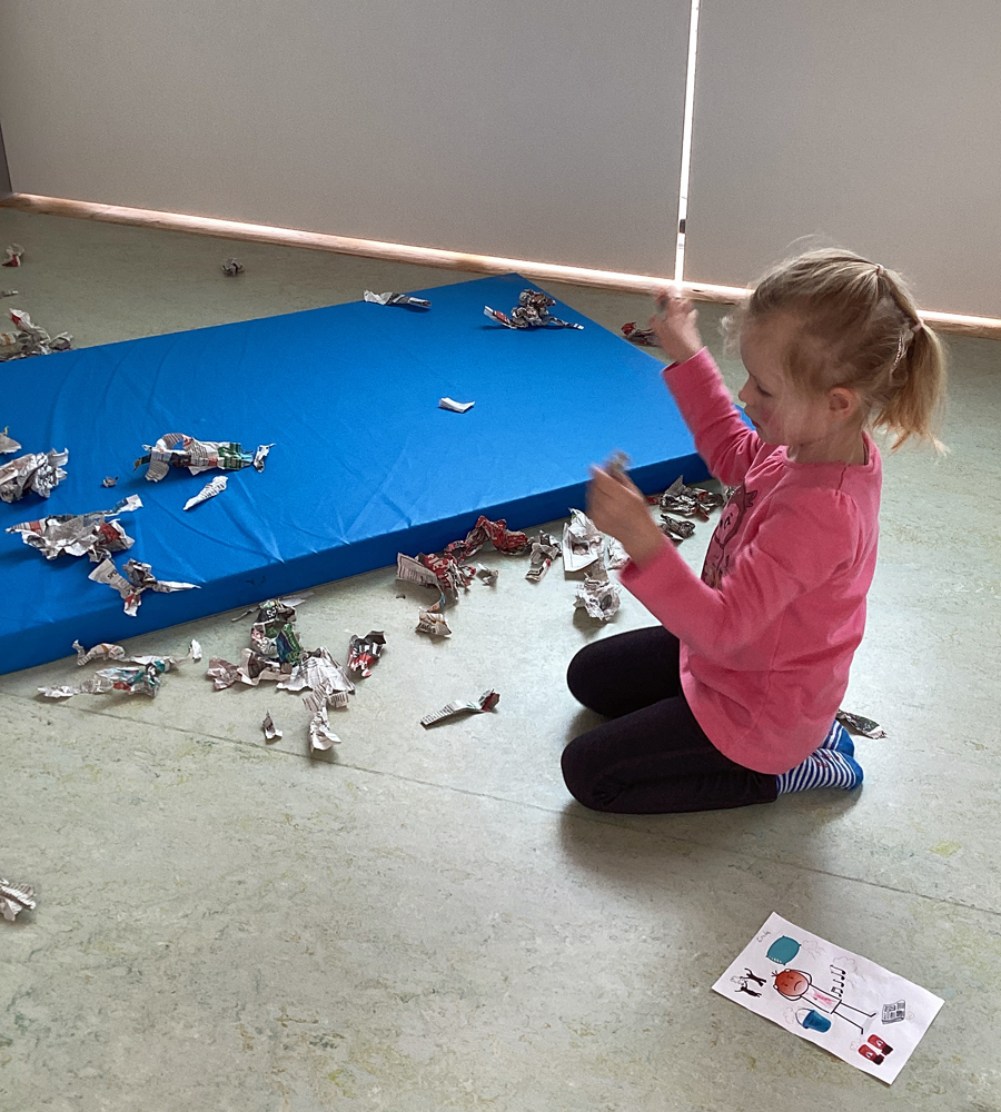 Ein Kind hockt auf dem Boden und zerreisst Papier in kleine Schnipsel