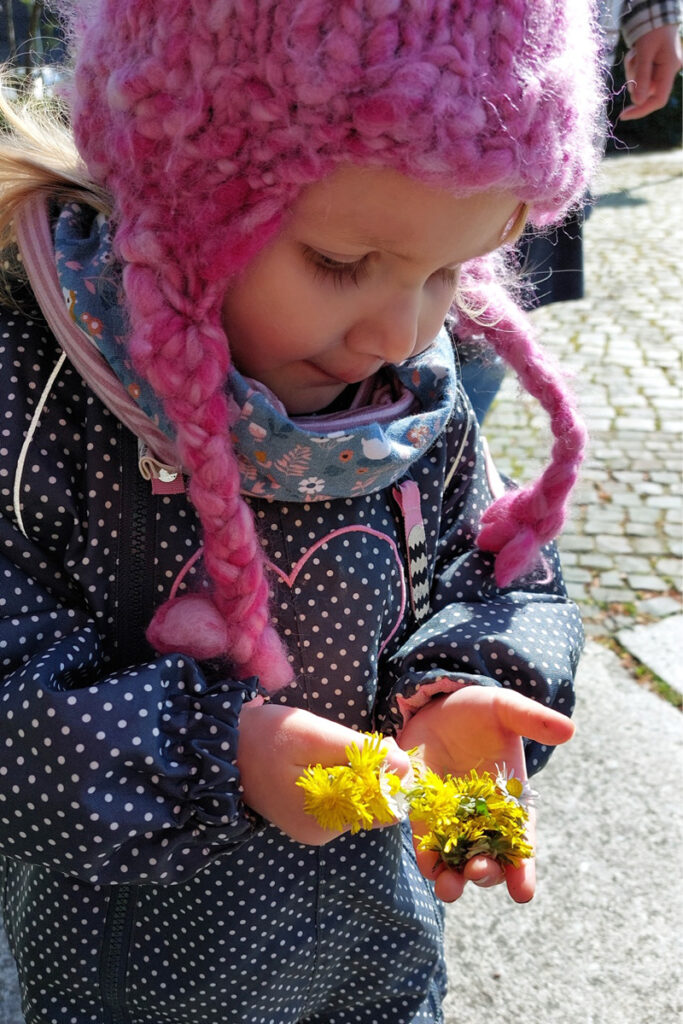 Ein Kind haelt gelbe Blueten in der Hand und sieht sie sich an