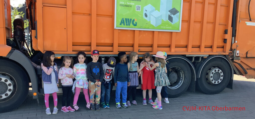 Kinder stehen vor einem grossen orangefarbenen Muellwagen der AWG Wuppertal