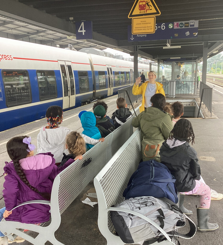 Kinder sitzen am Bahnsteig auf Metallbaenken