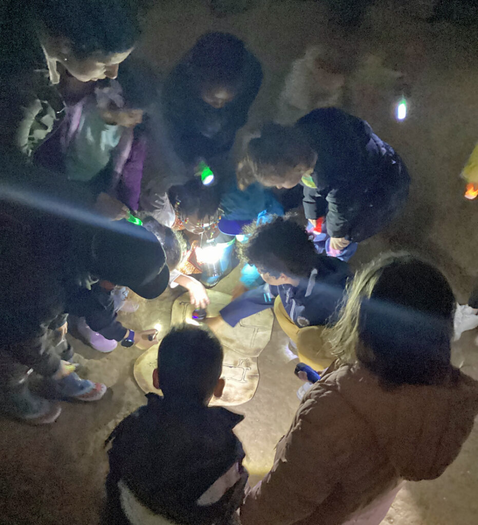 Mit Taschenlampen leuchten Kinder auf eine Schatzkarte in einer dunklen Hoehle