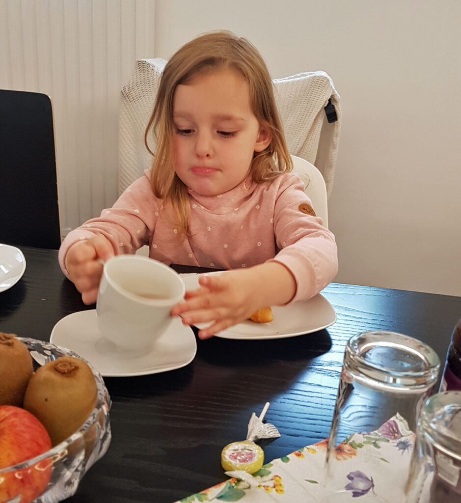 Ein Kind sitzt am Tisch und stellt eine Tasse wieder auf die Untertasse