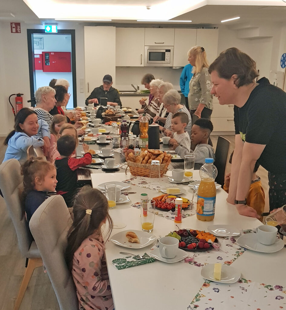 Kinder und aeltere Menschen sitzen zusammen am Tisch und fruehstuecken