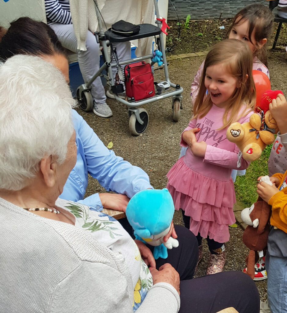 Kinder und Seniorinnen schauen sich Kuscheltiere an und sind froehlich