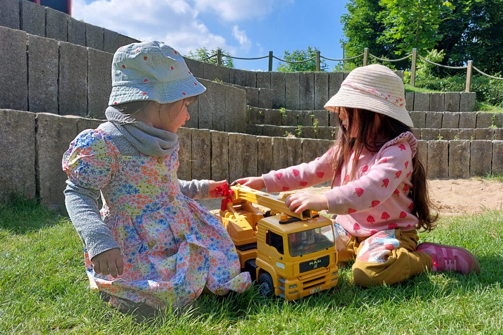 Zwei Maedchen spielen auf dem Rasen mit einem Spielzeuglaster