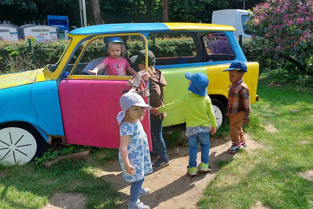 Kinder klettern in ein buntes Auto das auf einem Spielplatz steht