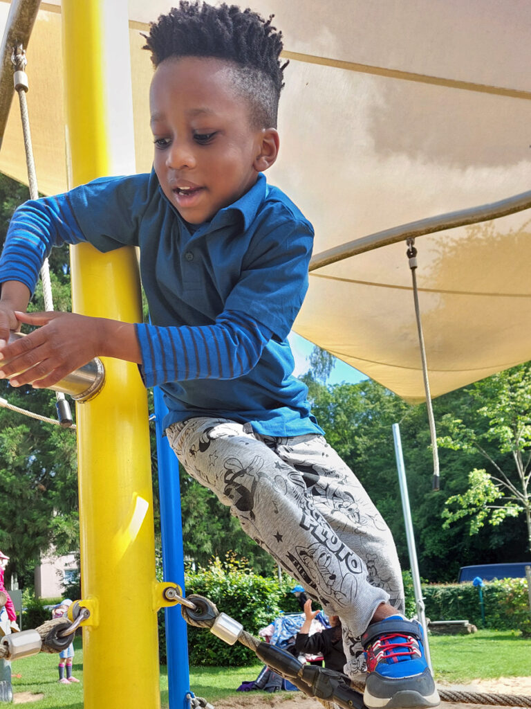 Ein Junge klettert auf ein Spielgeraet auf dem Spielplatz