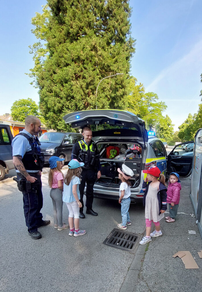 Zwei Polizisten zeigen Kinder ihr Dienstfahrzeug