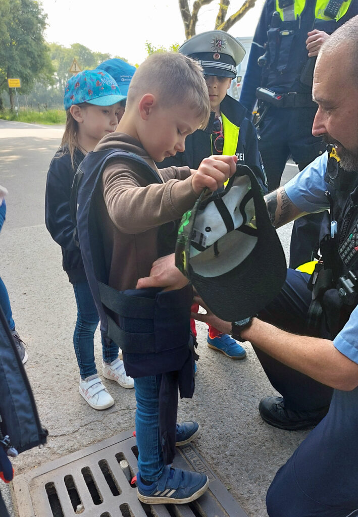 Ein Polizist laesst ein Kind seine Schutzweste anprobieren