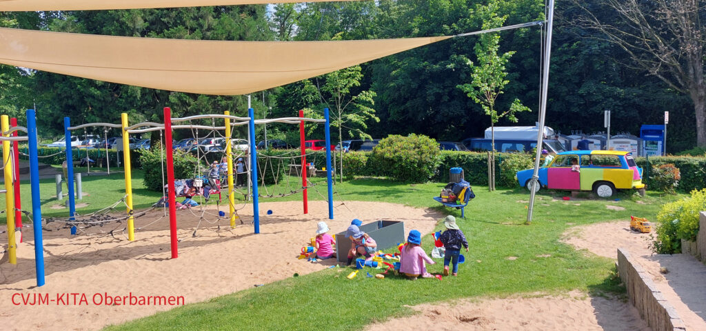 Kinder spielen auf einem grossen Spielplatz unter einem Sonnensegel