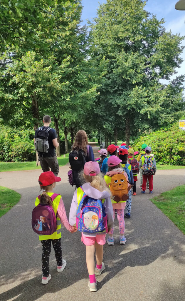 Eine Gruppe Kinder und Erwachsene spaziert in Velbert durch den schoenen Herminghauspark