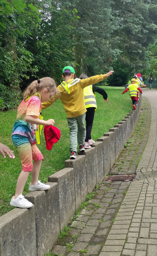 Kinder balancieren auf einer stufigen Mauer neben einem Weg im Herminghauspark