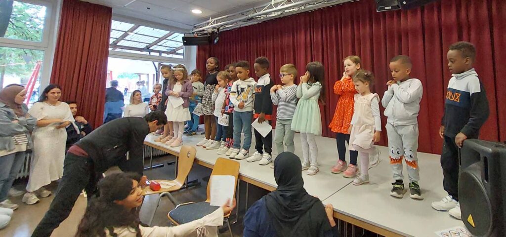 Kinder machen auf der Buehne Bewegungen zu einem Lied das sie singen