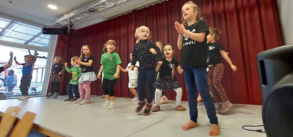 Kinder huepfen und klatschen auf der Buehne