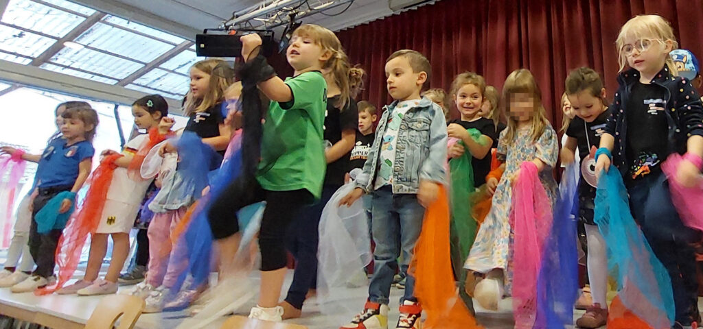 Kinder zeigen auf der Buehne einen Tanz mit bunten Tuechern