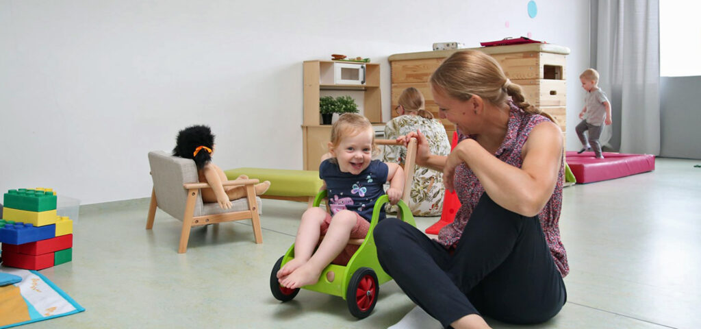 Kita-Kinder spielen im Beisein von Erwachsenen mit Fahrzeugen und auf Turnmatten