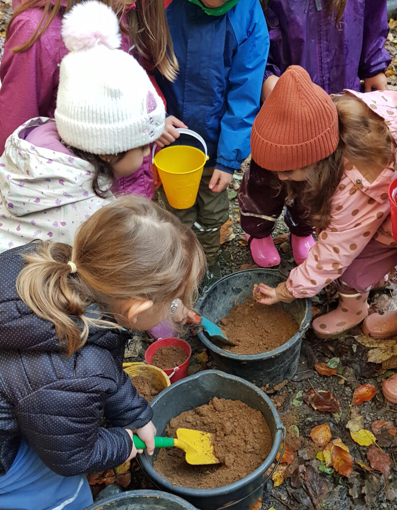 Kinder verruehren in schwarzen Eimern braune Erde mit Wasser