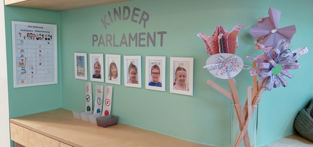 An einer Wand haengen Bilder mit Portraits von Kindern und darueber steht das Wort Kinderparlament