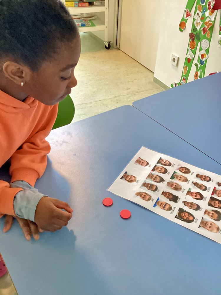 Ein Kind schaut sich ein Blatt Papier an auf dem die Gesichter von vielen Kindern zu sehen sind