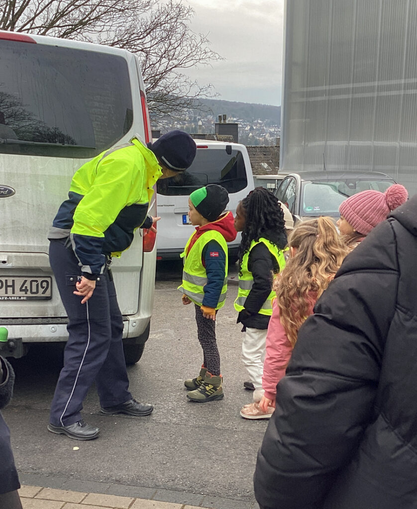 Kinder und Erwachsene schauen an einem geparkten Fahrzeug vorbei auf den Parkplatz