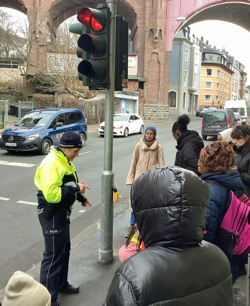 Eine Polizistin erklaert Kinder und Erwachsenen etwas an einer Fussgaengerampel