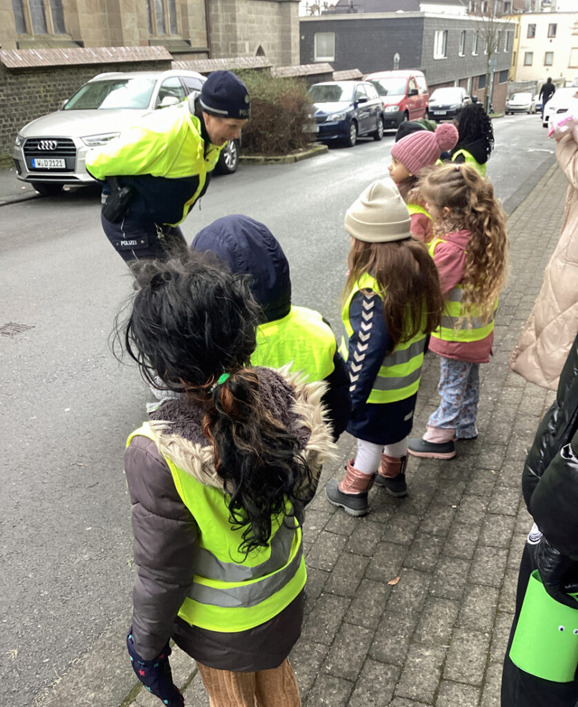 Eine Polizistin steht auf der Strasse und redet mit Kindern die auf dem Gehweg stehen