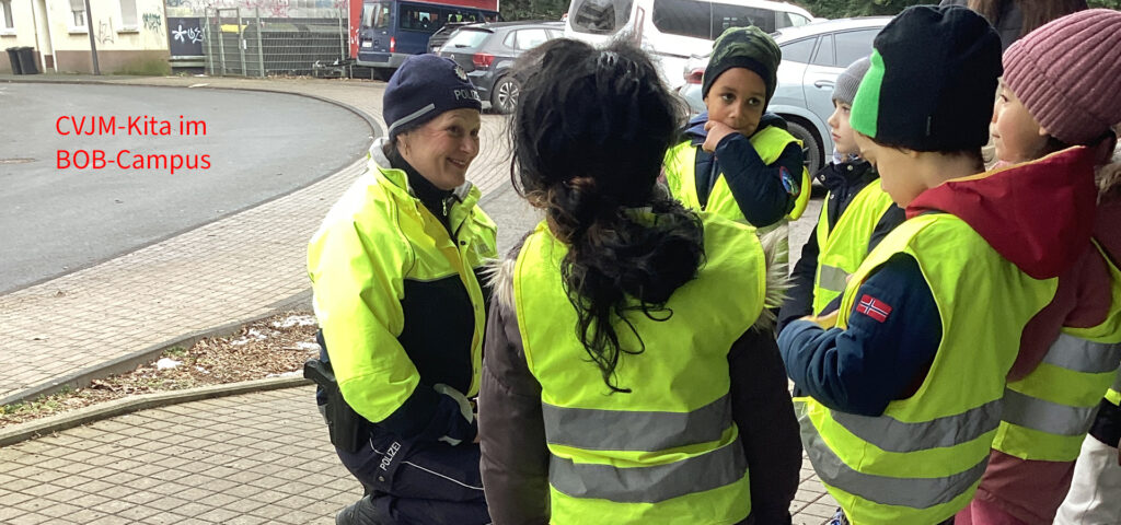 Kinder und eine Erwachsene stehen nahe einer Strasse und reden miteinander