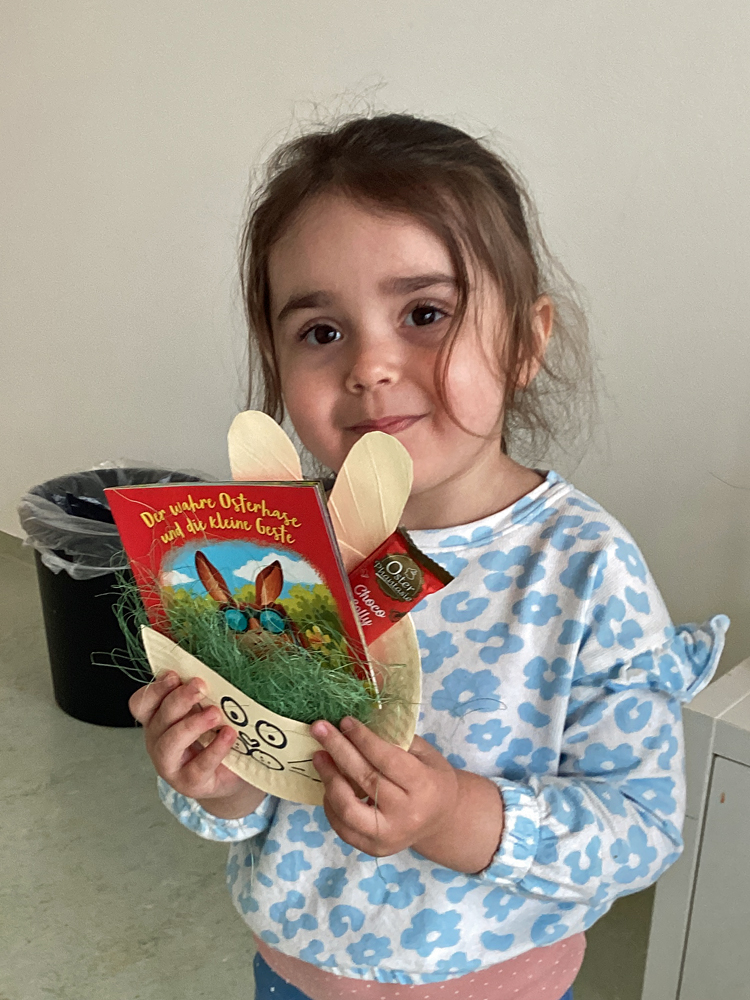 Ein Kind zeigt ein Osternest mit einem Buch und einem Schokololli