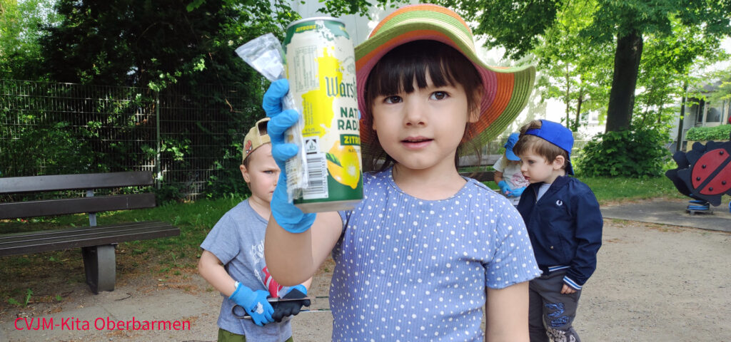 Ein Kind haelt auf einem Spielplatz eine leere Bierdose in die Hoehe