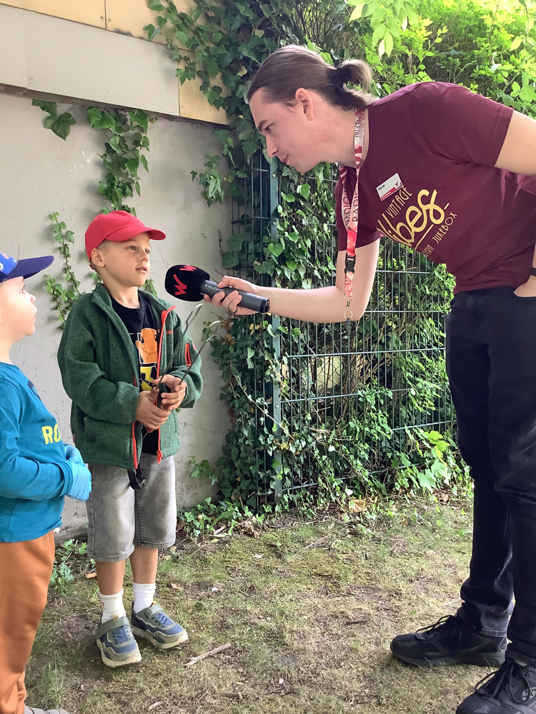 Ein Kind wird auf einer Wiese von einem jungen Mann mit Mikrophon interviewt