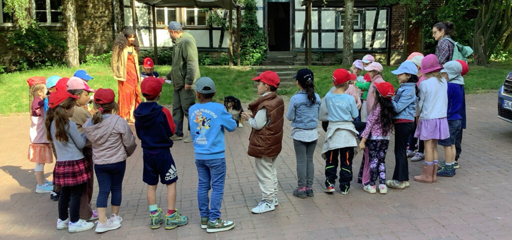 Eine Kindergruppe und zwei Erzieherinnen stehen vor einem Fachwerkhaus