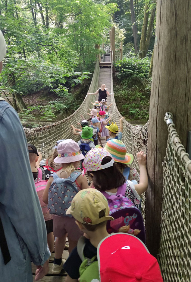 Kinder und Erwachsene gehen ueber die Haengebruecke im Zoo Wuppertal und halten sich an den Seitenwaenden fest
