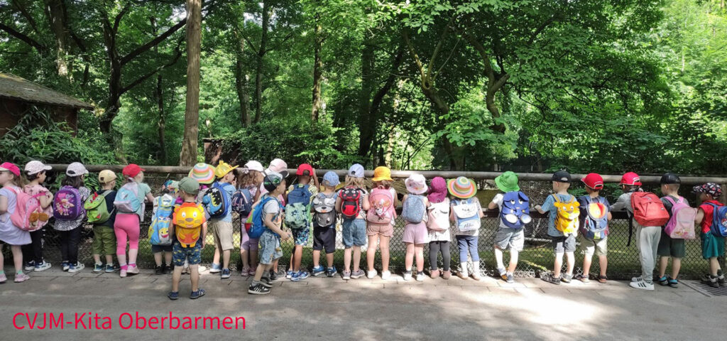 Kinder mit bunten Kopfbedeckungen stehen an einem Tiergehege im Wuppertaler Zoo