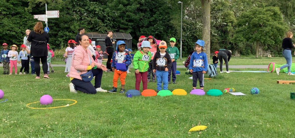 Kinder stehen draussen auf einer Wiese in Gruppen vor bunten Sportgeräten