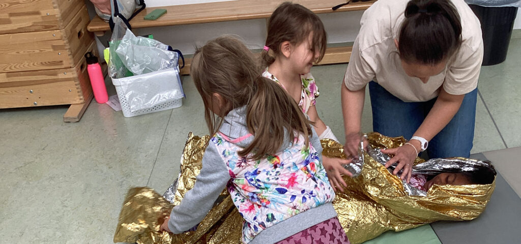 Kinder und die Kursleiterin ueben das Bergen einer verletzten Person