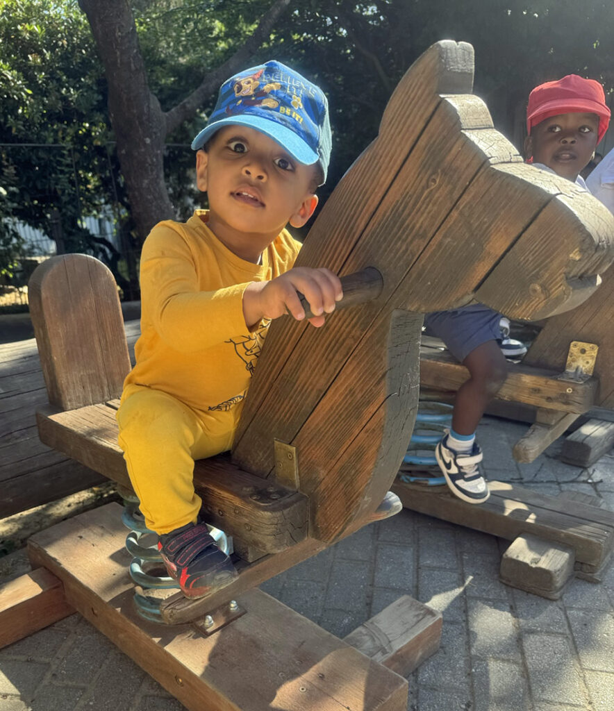 Kinder wippen auf Holzspieltieren draussen bei Sonnenschein