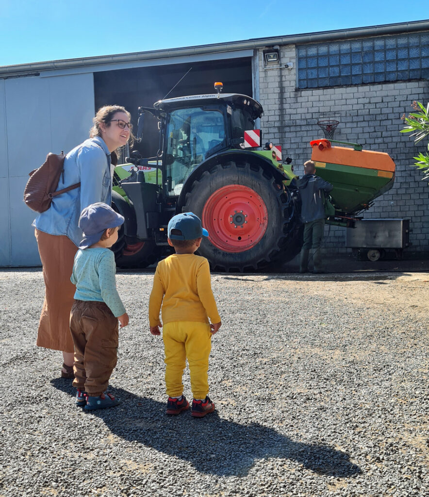 Kinder und eine Erzieherin schauen zu wie ein Mann einen grossen Traktor reinigt