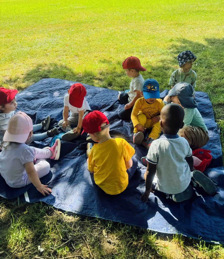Kinder sitzen auf einer grossen blauen Picknickdecke im Schatten
