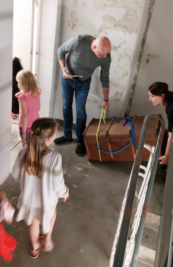Ein Erzieher und eine Erzieherin tragen eine grosse Schatzkiste vom Treppenhaus in einen Raum