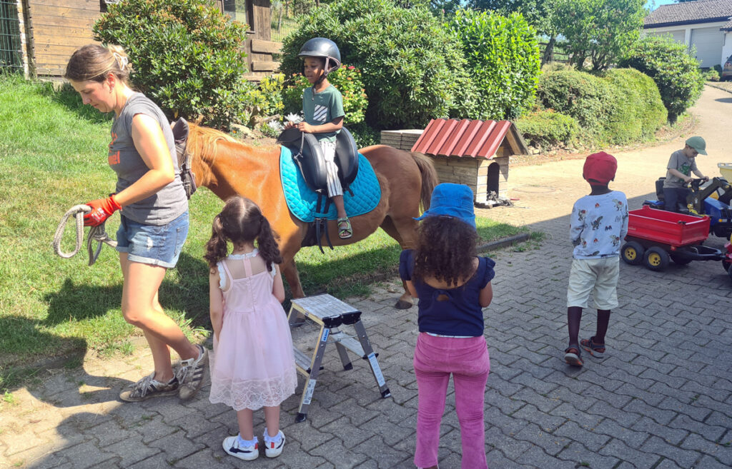 Ein Kind reitet auf einem Pony und andere Kinder schauen zu